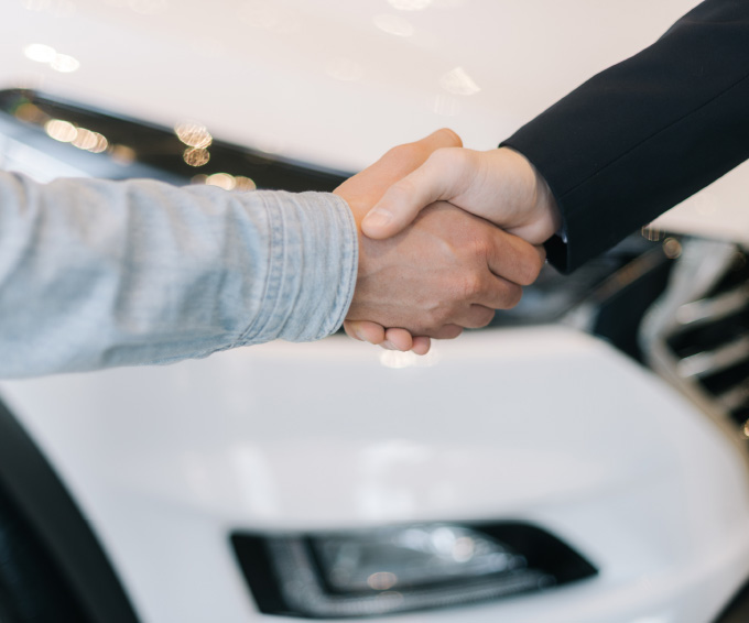 Vorteile Zwei Personen geben sich die Hand vor einem Auto.